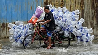 Un hombre utiliza su bicitaxi para transportar contenedores de plástico usados por una calle inundada en la ciudad de Valenzuela, Filipinas, agosto de 2023. 