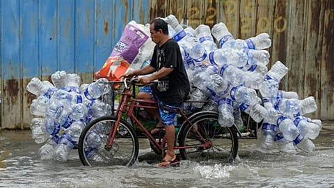 Un hombre utiliza su bicitaxi para transportar contenedores de plástico usados por una calle inundada en la ciudad de Valenzuela, Filipinas, agosto de 2023. 