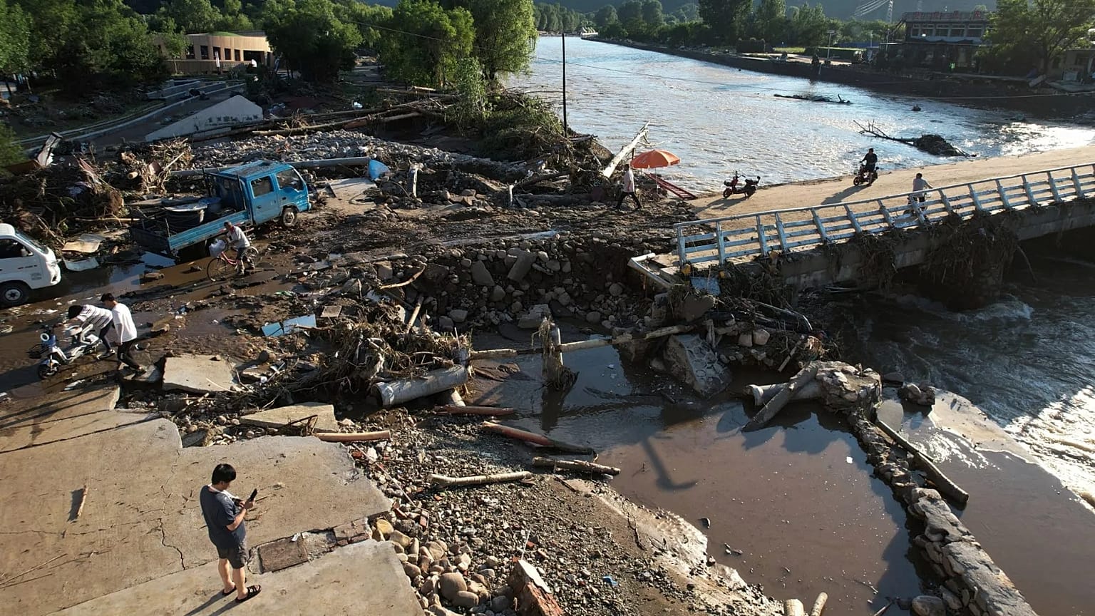 Pessoas atravessam uma margem de rio danificada após uma inundação repentina no distrito de Jizhou, em Tianjin, a 29 de julho de 2025