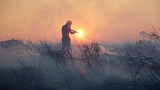 Um bombeiro tenta extinguir as chamas durante um incêndio florestal, no subúrbio de Kryoneri, no noroeste de Atenas, Grécia, a 26 de julho.