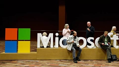 Attendees of Microsoft Corp.'s annual shareholders meeting sit on a Microsoft sign while waiting for the meeting to begin. December 2014.