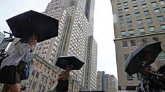 Fußgänger nutzen Regenschirme, während sie am Donnerstag, dem 31. Juli 2025, während eines Regenschauers am Empire State Building in New York vorbeigehen.
