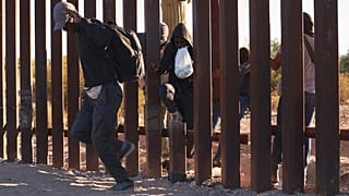 Illegális bevándorlók jutnak be az Egyesült Államokba a mexikói határkerítésen levő résen át az arizonai Lukeville településnél 2023. december 12-én