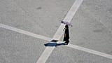 Archive (02.08.2025): A woman uses an umbrella to shield herself from the sun as she crosses Lisbon's Praça do Comércio on a hot day