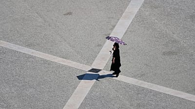 Archive (02.08.2025): A woman uses an umbrella to shield herself from the sun as she crosses Lisbon's Praça do Comércio on a hot day