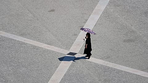Archive (02.08.2025): A woman uses an umbrella to shield herself from the sun as she crosses Lisbon's Praça do Comércio on a hot day.