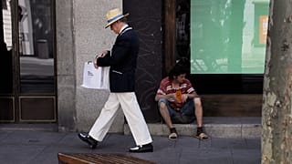 Un hombre pide dinero mientras un transeúnte mira dentro de una bolsa de compras en Madrid, el martes 6 de agosto de 2013.