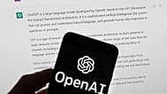 The OpenAI logo is seen on a mobile phone in front of a computer screen which displays output from ChatGPT, March 21, 2023, in Boston