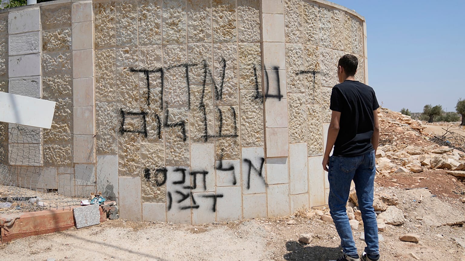 رجل فلسطيني يتفقد كتابات بالعبرية تقول "تحية من ديفيد شالون، لا تغطوا دمه"، في بلدة رمّون بالضفة الغربية، شرقي رام الله، الخميس تموز 2025