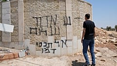 رجل فلسطيني يتفقد كتابات بالعبرية تقول "تحية من ديفيد شالون، لا تغطوا دمه"، في بلدة رمّون بالضفة الغربية، شرقي رام الله، الخميس تموز 2025