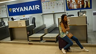 Uma mulher senta-se numa mala junto a um balcão de check-in da companhia aérea Ryanair no aeroporto internacional de Madrid, a 25 de julho de 2018.