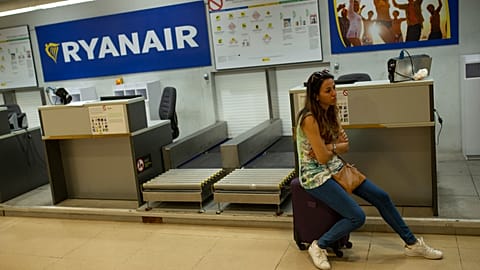 Kobieta siedzi na walizce obok stanowiska odprawy linii lotniczych Ryanair na międzynarodowym lotnisku w Madrycie, 25 lipca 2018 r.