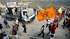 Colonos seguram uma bandeira cor de laranja, a cor adoptada pelos opositores ao plano de retirada dos colonos da Faixa de Gaza, enquanto famílias de Gaza chegam à Cisjordânia, terça-feira, 14 de junho de 2005.