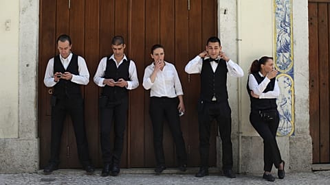Waiter Joao Sintra, second right, adjusts his tie as waitress Maria Almas, center, smokes a cigarette during a break with co-workers in downtown Lisbon. 27 April 2013.
