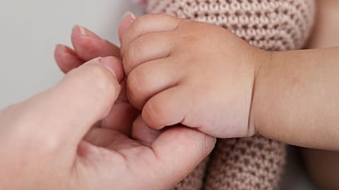 A parent holds their baby's hand.