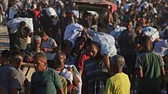 يحمل فلسطينيون طرودًا غذائية من قافلة مساعدات إنسانية تحركت على طول ممر موراج بالقرب من رفح، في جنوب قطاع غزة، يوم الاثنين 4 أغسطس/آب 2025. 