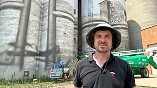 Artist Guido van Helten poses for a photo in front of the grain elevator and silos where he is painting a large mural.