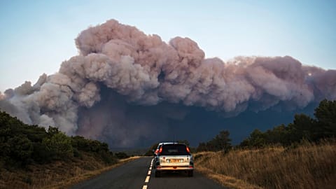 Cars drive past a fast-moving wildfire in a Mediterranean region of France near the Spanish border is pictured Tuesday Aug.5, 2025.