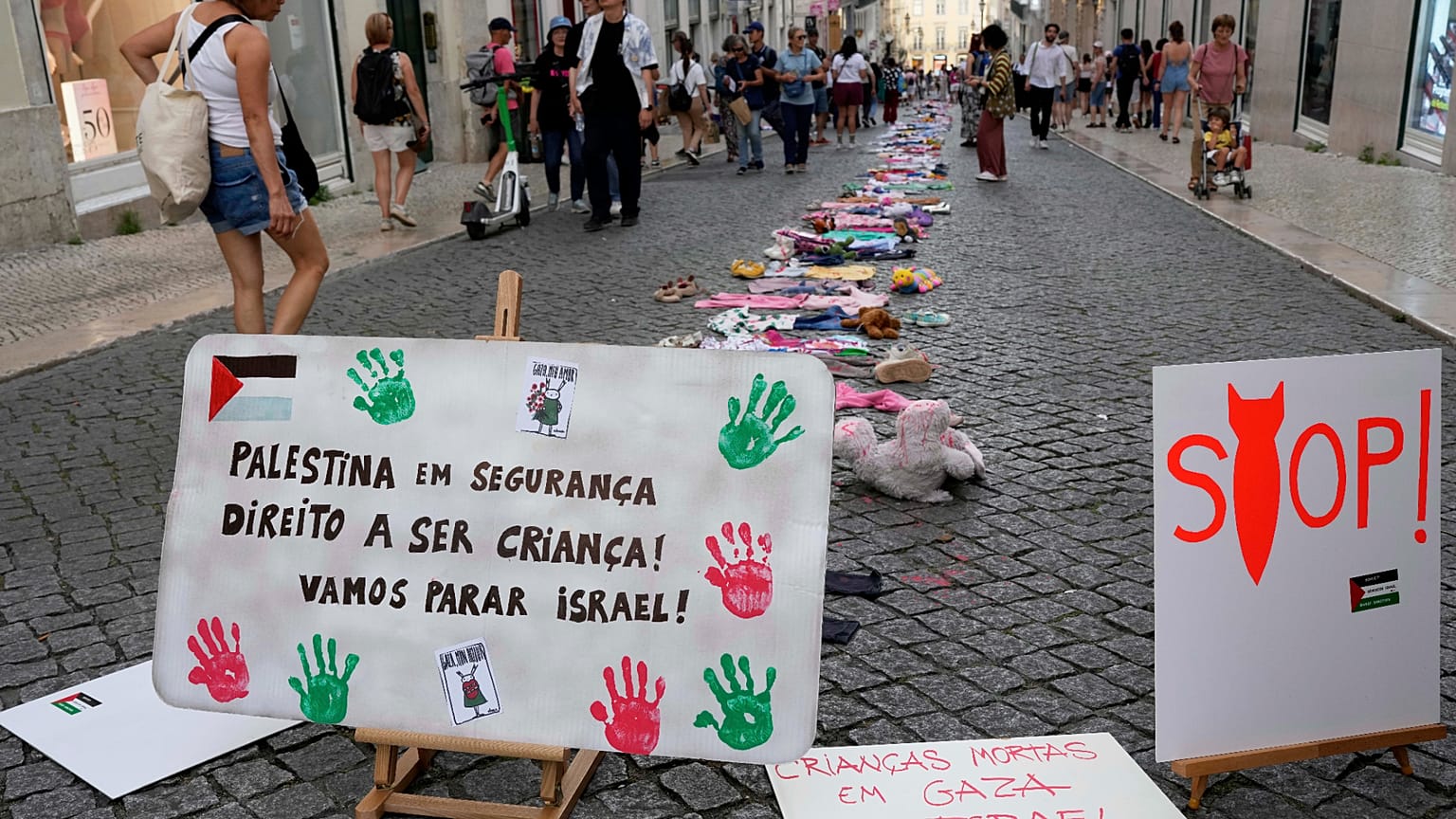Un grupo de personas pasa junto a una instalación de ropa y juguetes infantiles en la Rua do Carmo, en el centro de Lisboa, para llamar la atención sobre la situación de los niños en Gaza.