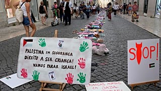 Pessoas passam por uma instalação de roupas e brinquedos infantis espalhados pela rua do Carmo, no centro de Lisboa, para chamar a atenção para a situação das crianças em Gaza