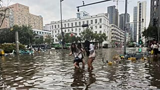 Mulheres atravessam uma estrada inundada na sequência de fortes chuvadas em Zhengzhou, 7 de agosto de 2025