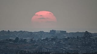 O sol põe-se atrás de edifícios destruídos durante as operações terrestres e aéreas israelitas no norte da Faixa de Gaza, visto do sul de Israel, 8 de agosto de 2025.
