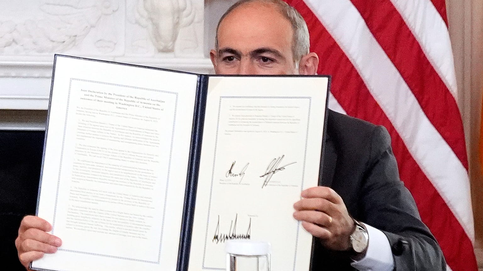 O primeiro-ministro da Arménia, Nikol Pashinyan, segura um acordo trilateral assinado durante uma cerimónia com o presidente do Azerbaijão, Ilham Aliyev, e o presidente Donald Trump, 8 de agosto de 2025