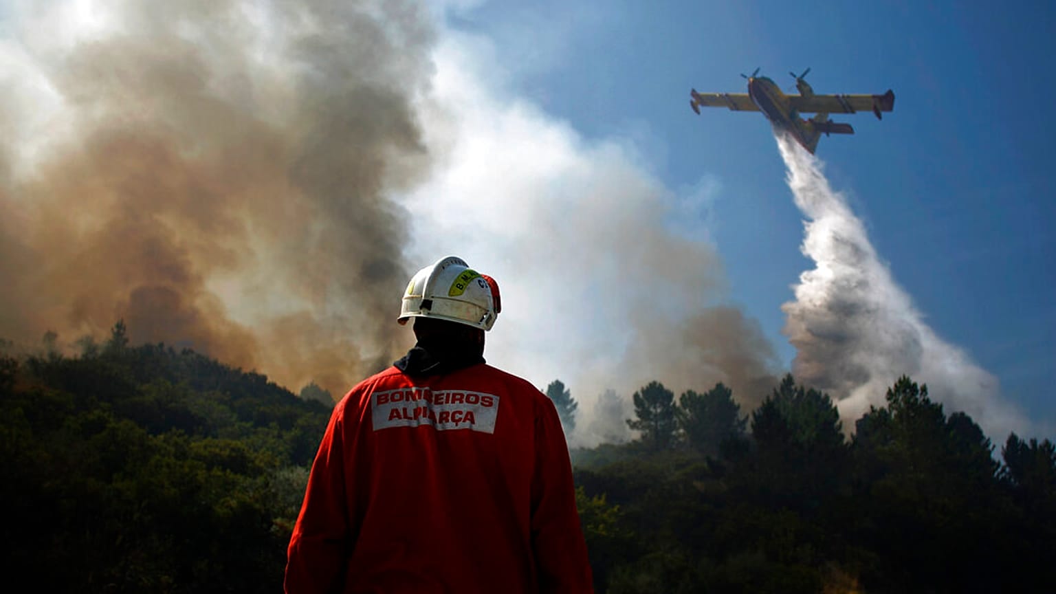 ARQUIVO (23/08/2013): Um bombeiro português está de pé enquanto um avião de bombardeamento de água espalha água para extinguir um incêndio em Adsamo, perto de Vouzela.