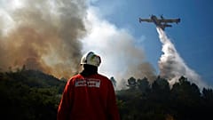 ARQUIVO (23/08/2013): Um bombeiro português está de pé enquanto um avião de bombardeamento de água espalha água para extinguir um incêndio em Adsamo, perto de Vouzela.
