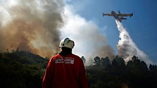 ARQUIVO (23/08/2013): Um bombeiro português está de pé enquanto um avião de bombardeamento de água espalha água para extinguir um incêndio em Adsamo, perto de Vouzela.