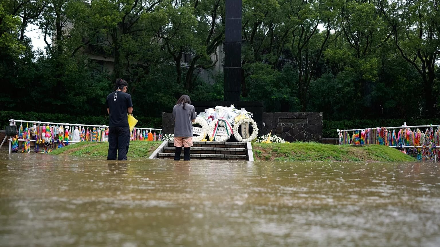 Duas pessoas rezam com água até aos joelhos num memorial em homenagem às vítimas do bombardeamento atómico em Nagasaki, 9 de agosto de 2025