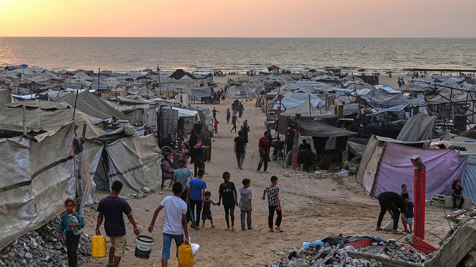 نازحون فلسطينيون يسيرون عبر مخيم مؤقت على طول الشاطئ في مدينة غزة، الأحد 10 أغسطس/آب 2025.