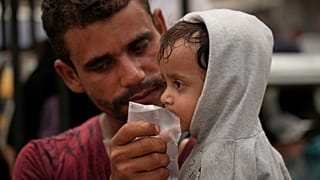 رجل يسقي طفلاً ماءً من كيس بلاستيكي اشتراه للتو مقابل شيكل واحد، في مدينة غزة، الثلاثاء 12 أغسطس 2025