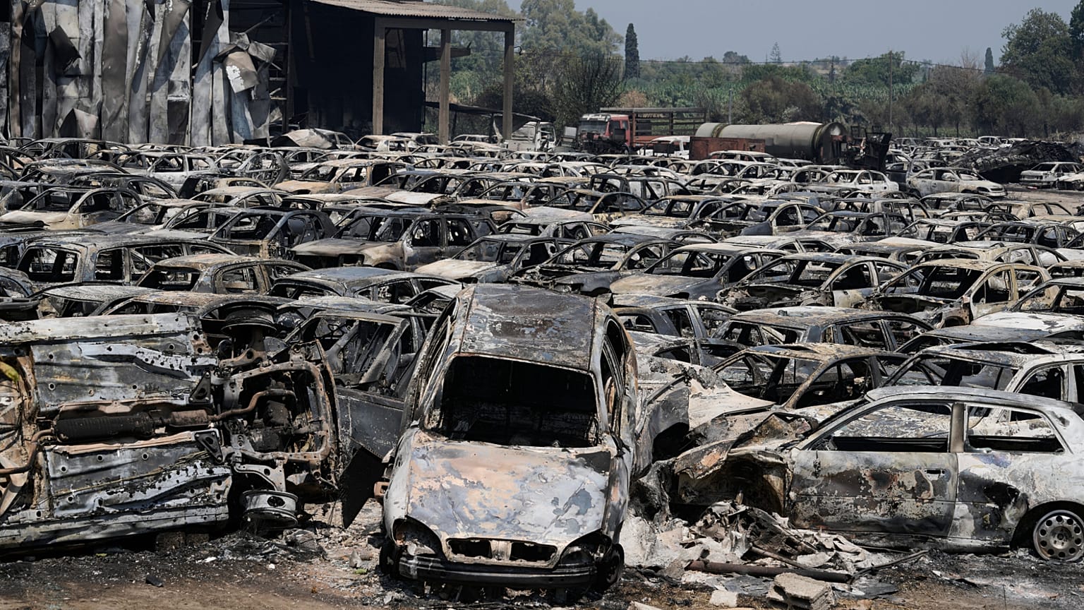 Des voitures brûlées sont visibles dans un parc de fourrière à Kato Achaia, lors d'un incendie de forêt près de la ville de Patras, dans l'ouest de la Grèce, mercredi 13 août 2025