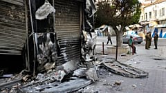 جنود من الجيش السوري، على اليمين، يقفون حراسًا بجوار متجر أُحرق خلال اشتباكات بين قوات الأمن وجماعات مسلحة في اللاذقية، شمال غرب دمشق، سوريا، يوم الأحد 27 مارس/آذار 2011. 