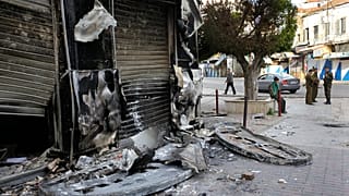 جنود من الجيش السوري، على اليمين، يقفون حراسًا بجوار متجر أُحرق خلال اشتباكات بين قوات الأمن وجماعات مسلحة في اللاذقية، شمال غرب دمشق، سوريا، يوم الأحد 27 مارس/آذار 2011. 