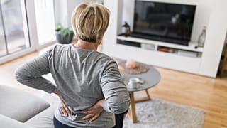 A woman clutches her lower back in pain.