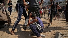 طفل فلسطيني ينحني بعد تعرضه لضربة على رأسه بينما يهرع الناس لجمع المساعدات الإنسانية التي أسقطتها المظلات على مدينة غزة، شمال قطاع غزة، الخميس 14 أغسطس/آب 2025.