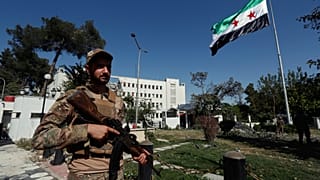 جنود سوريون يرفعون العلم السوري أمام مبنى وزارة الدفاع الذي تعرض لغارات جوية إسرائيلية، في دمشق، سوريا، السبت 19 يوليو/ تموز 2025.