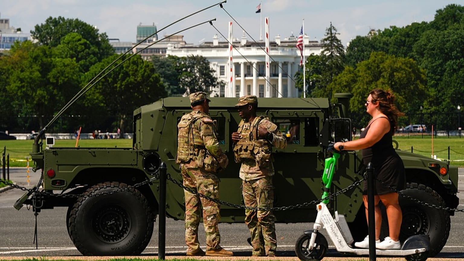 Miembros de la Guardia Nacional del Distrito de Columbia patrullan frente a la Casa Blanca mientras una mujer pasa en scooter, el sábado 16 de agosto de 2025, en Washington.