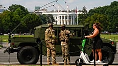 A Columbia Kerületi Nemzeti Gárda tagjai járőröznek a Fehér Ház előtt, miközben egy nő robogón halad el mellettük 2025. augusztus 16-án, szombaton Washingtonban.