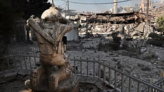Vêm-se lojas destruídas em frente a uma estátua de um combatente do Hezbollah numa rua comercial que foi atingida na noite de sábado por ataques aéreos israelitas no sul do Líbano, 13 de outubro de 2024