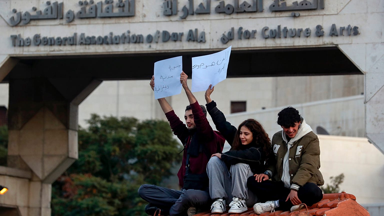 نشطاء سوريون يحملون لافتات باللغة العربية كتب عليها:" الفن صوت الحرية "، و"سوريا دولة ديمقراطية ومدنية" ، على اليسار ، خلال احتجاج للمطالبة بدولة علمانية  19 ديسمبر 2024