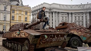 Um rapaz senta-se em cima de um tanque russo danificado exposto no centro de Kiev, na Ucrânia. março de 2025.