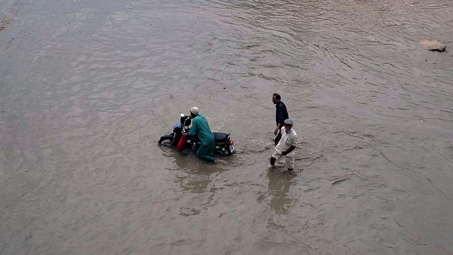 Pessoas atravessam uma estrada inundada após fortes chuvas em Karachi, Paquistão, na terça-feira, 19 de agosto de 2025