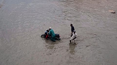 People navigate through a flooded road after heavy rainfall in Karachi, Pakistan, Tuesday, Aug. 19, 2025.