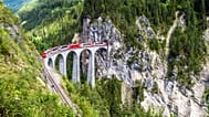 Vista aérea de un puente ferroviario y un tren rojo en Suiza. 