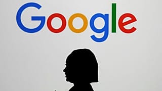 A woman walks by a giant screen with a logo at an event at the Paris Google Lab on the sidelines of the AI Action Summit in Paris, on Feb. 9, 2025. 