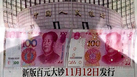 In this Aug. 11, 2015 photo, a shadow of a man is reflected on a glass as he reads a newspaper reporting China's central bank, the People's Bank of China.