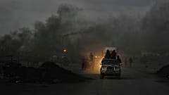 فلسطينيون يقودون سياراتهم وسط دخان أسود من مواقد مؤقتة تستخدم لاستخراج الوقود من البلاستيك المذاب على طول طريق البحر، عند الغسق في جنوب مدينة غزة